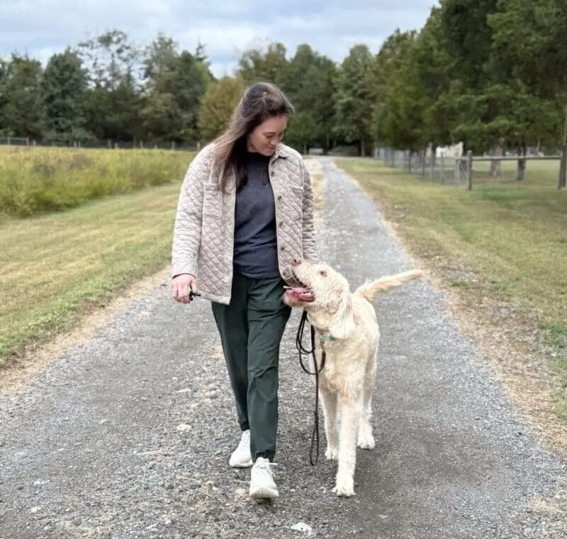 Woman walking a golden retriever on a gravel path in a park.