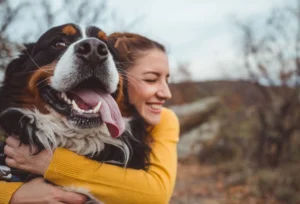 Woman joyfully hugging her happy dog outdoors.